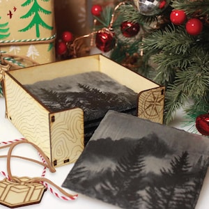 a wooden box with a carved design, a set of coasters with a mountain landscape, and a Christmas tree with red ornaments.