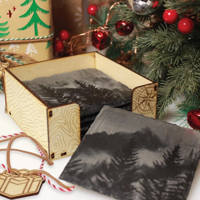 a wooden box with a carved design, a set of coasters with a mountain landscape, and a Christmas tree with red ornaments.
