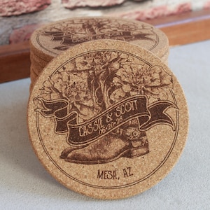 Puede incluir: Un conjunto de posavasos redondos de corcho con un diseño grabado con láser. Cada posavasos presenta una bota de vaquero, flores y una pancarta con los nombres "CASSIE & SCOTT" y la fecha "06-20-26". La ciudad "MESA, AZ" también está grabada.