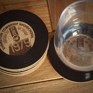 May include: A set of six black and brown cork coasters with a vinyl record design. The coasters feature the text "Evanston Township High School Cheers to Class of 1975 50 Years".