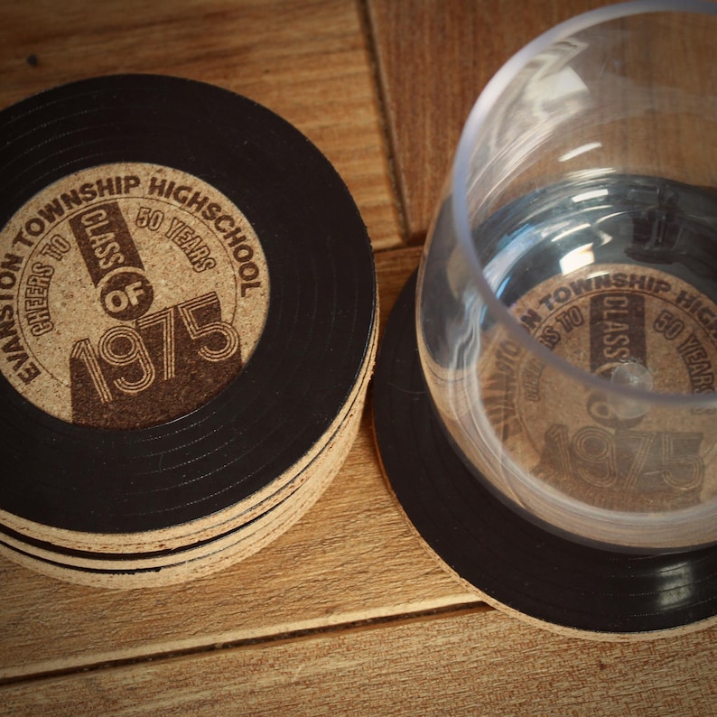 May include: A set of six black and brown cork coasters with a vinyl record design. The coasters feature the text "Evanston Township High School Cheers to Class of 1975 50 Years".