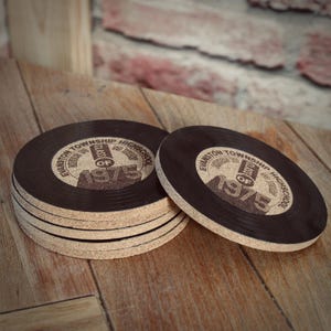 May include: Six brown cork coasters with a black vinyl record design. The coasters feature the text "Evanston Township High School" and "Class of 1975".