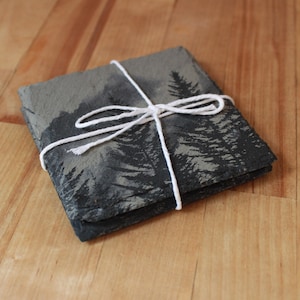 Slate stone drink coaster featuring graphic of a foggy mountain scene etched onto the top surface of the coaster