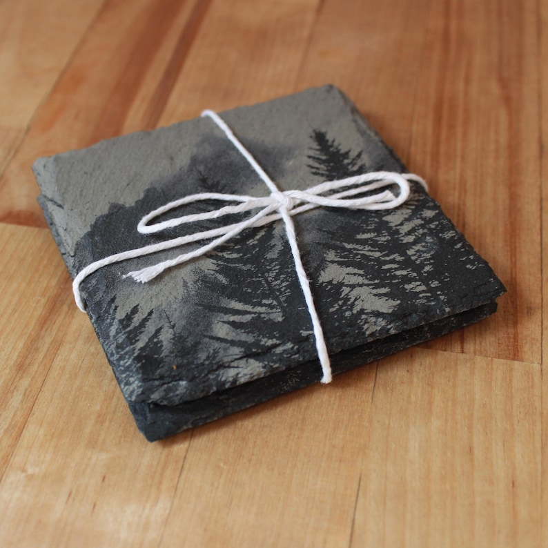 Slate stone drink coaster featuring graphic of a foggy mountain scene etched onto the top surface of the coaster