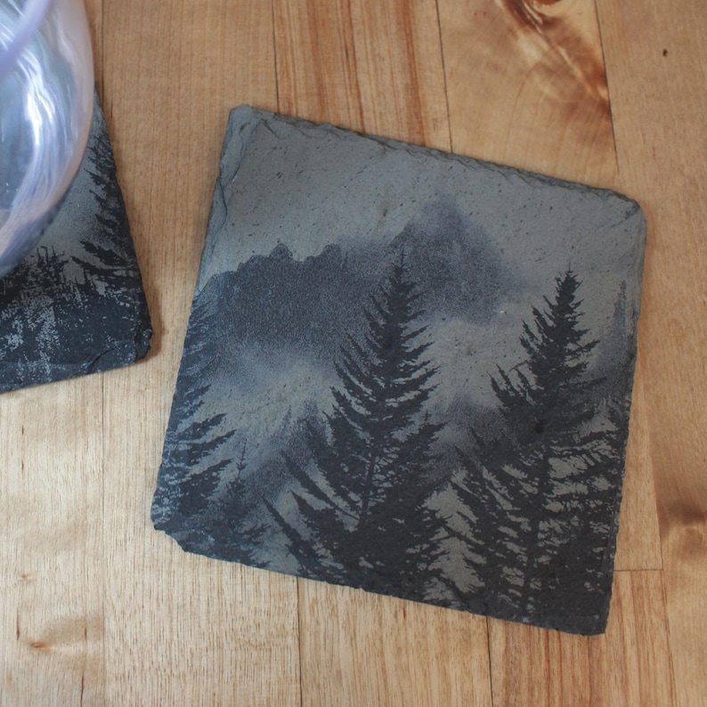 Slate stone drink coaster featuring graphic of a foggy mountain scene etched onto the top surface of the coaster