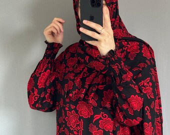 May include: Black and red floral patterned dress and hijab. The dress features long sleeves with gathered cuffs. The floral design is a repeating pattern of red flowers on a black background. The hijab matches the dress.