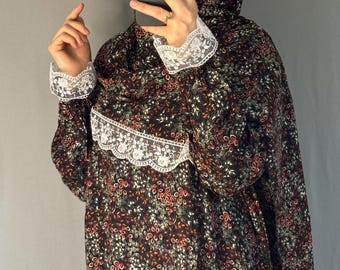 May include: A dark floral print garment with white lace trim. The fabric features a pattern of red, white, and green flowers on a black background. The garment has long sleeves and a hood.