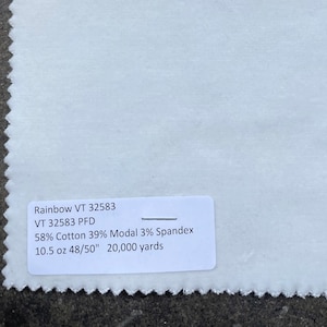 Puede incluir: Una muestra de tela blanca con una etiqueta que dice "Rainbow VT 32583 VT 32583 PFD 58% Algodón 39% Modal 3% Spandex 10.5 oz 48/50" 20.000 yardas"