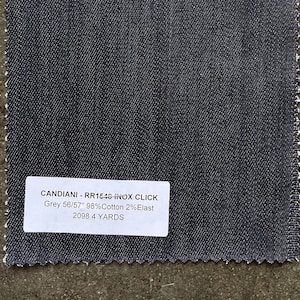May include: A close-up of a dark gray fabric swatch with a white label that reads "CANDIANI - RR1546 INOX CLICK Grey 56/57" 98% Cotton 2% Elast 2098.4 YARDS".