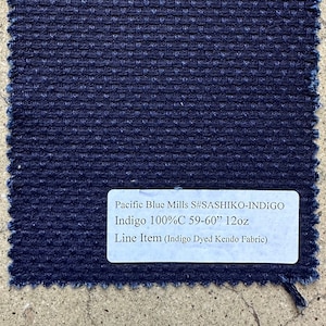 May include: A close-up of a dark blue fabric swatch with a white label that reads "Pacific Blue Mills S#SASHIKO-INDIGO Indigo 100%C 59-60" 12oz Line Item (Indigo Dyed Kendo Fabric)"