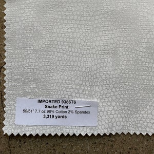 Op de afbeelding: Een witte stofstaal met een slangenprint. De stof is 50/51 inch breed en weegt 7,7 ounce per yard. Het is gemaakt van 98% katoen en 2% spandex. De stof is 3.319 yard lang.