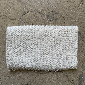 May include: A white, textured fabric swatch with a slightly frayed edge.