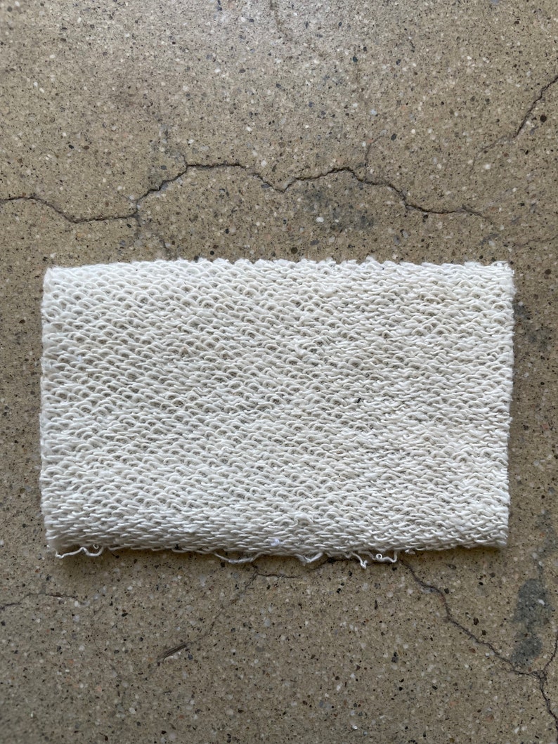May include: A white, textured fabric swatch with a slightly frayed edge.