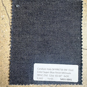 May include: A dark blue denim fabric swatch with a white label that reads "Candiani Italy S# RR6716-SM Elast Color Super Blue finish Millinum 98%C 2%E 12oz 65-63" 3x1R 4,660 Yards SA51-SB41"