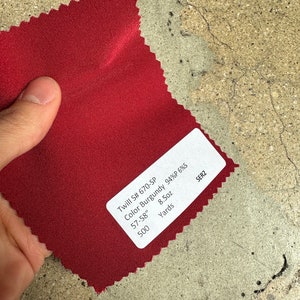 May include: A burgundy twill fabric swatch with a label that reads "Twill S# 670-SP Color Burgundy 94%P 6%S 57-58" 8.5oz 500 Yards SER2"