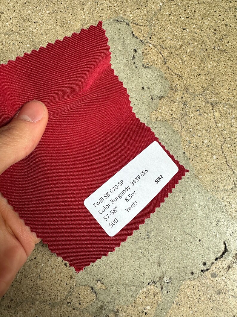 May include: A burgundy twill fabric swatch with a label that reads "Twill S# 670-SP Color Burgundy 94%P 6%S 57-58" 8.5oz 500 Yards SER2"