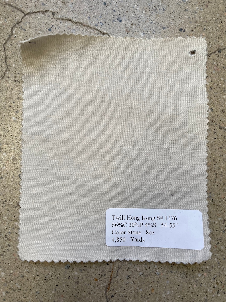 May include: A close-up of a beige twill fabric swatch with a label that reads "Twill Hong Kong S# 1376 66%C 30%P 4%S 54-55" Color Stone 8oz 4,850 Yards".