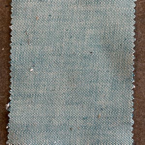 May include: A square fabric swatch with a teal and white diagonal weave pattern. The edges are cut with a zig-zag pattern. The fabric has a textured appearance with small flecks of color throughout. The swatch is likely for textiles or crafting.