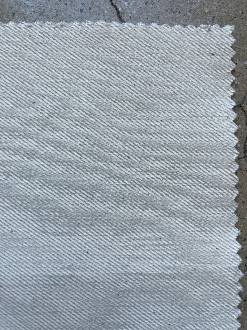 Puede incluir: Primer plano de una tela blanca con un sutil patr&oacute;n de tejido diagonal. La tela tiene una textura ligeramente rugosa.