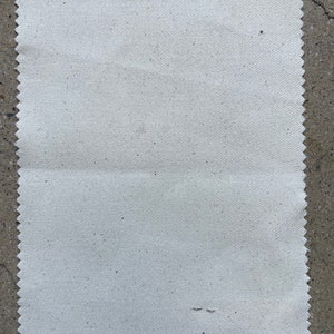 Puede incluir: Una muestra de tela blanca lisa con una superficie ligeramente texturizada. La tela tiene un borde festoneado.