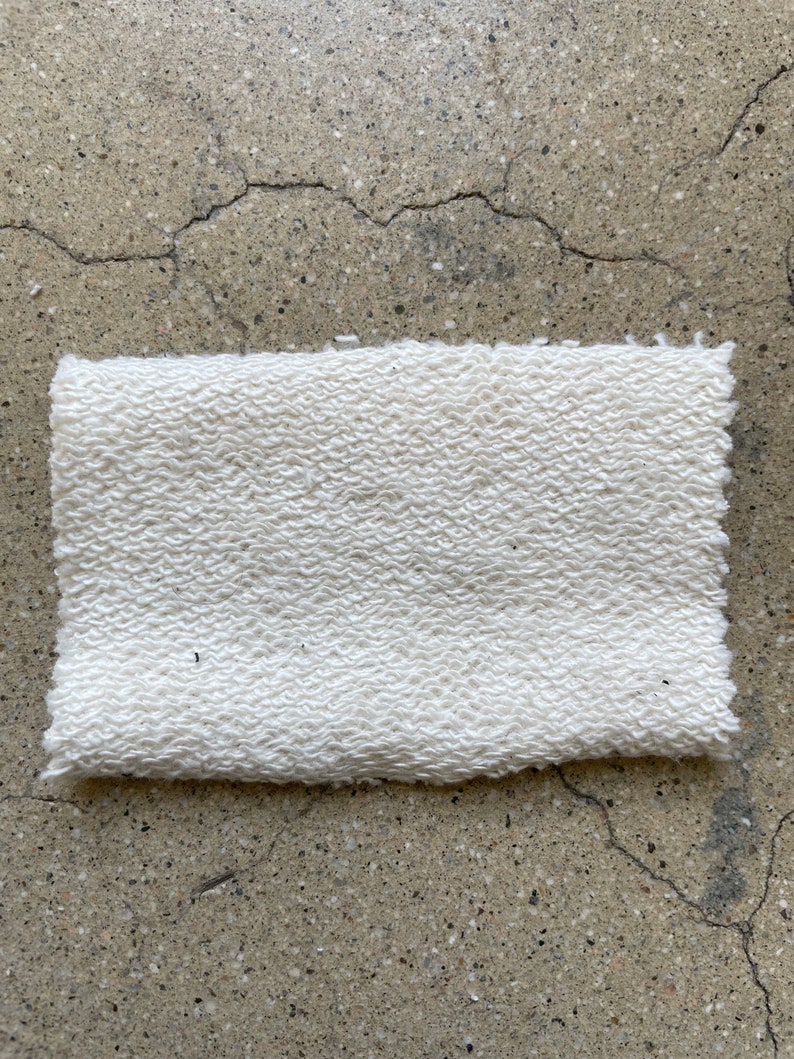 May include: A white, textured fabric swatch. The fabric has a slightly bumpy texture.