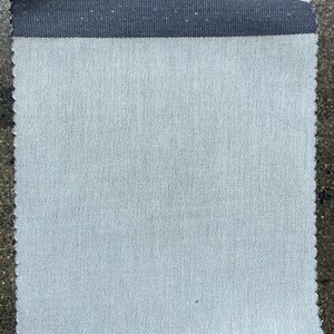 May include: A close-up of a light gray fabric with a black woven trim. The fabric has a subtle diagonal weave pattern.