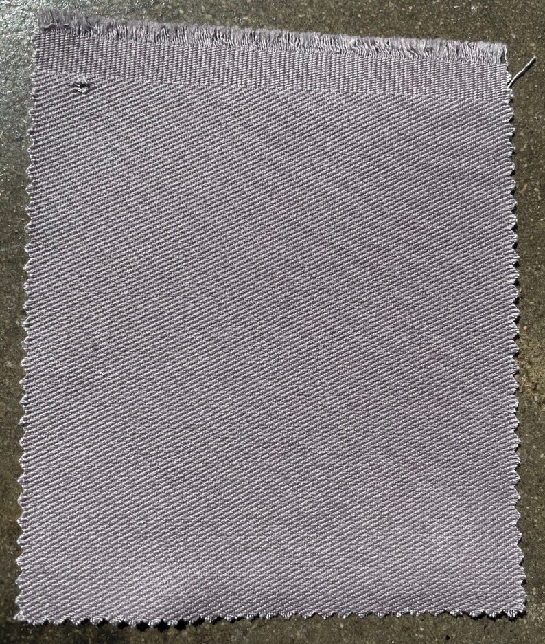 Op de afbeelding: Een close-up van een stuk lichtgrijs stof met een subtiel diagonaal weefpatroon.