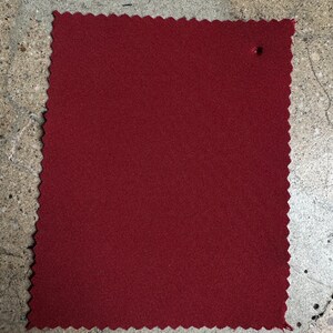 May include: A close-up of a solid burgundy fabric swatch. The fabric has a subtle texture and a slightly scalloped edge.
