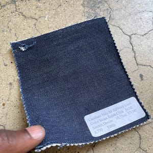 May include: A dark blue denim fabric swatch with a white label that reads "Candiani Italy S# RR9648 Elast Color Sioux finish Click 3x1R Stretch Denim 10.75oz 57-58" 6,770 Yards"