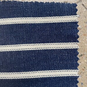 Puede incluir: Primer plano de una tela azul marino con rayas blancas. La tela tiene una superficie texturizada y un borde ligeramente irregular.