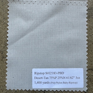 Puede incluir: Una muestra de tela beige claro con una etiqueta blanca que dice "Ripstop S#J2183-PBD Desert-Tan 75%P 25%N 61/62" 3oz 1.400 yardas (Poly/Nylon Baby-Ripstop)"