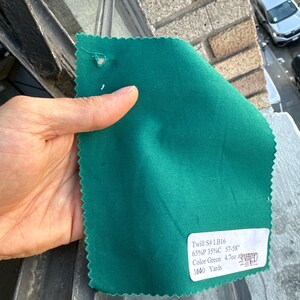 May include: A swatch of green twill fabric with a label that reads "Twill S# LB16 65%P 35%C 57-58" Color Green 4.7oz 1040 Yards"