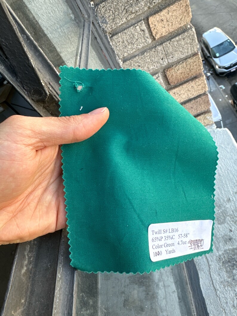 May include: A swatch of green twill fabric with a label that reads "Twill S# LB16 65%P 35%C 57-58" Color Green 4.7oz 1040 Yards"