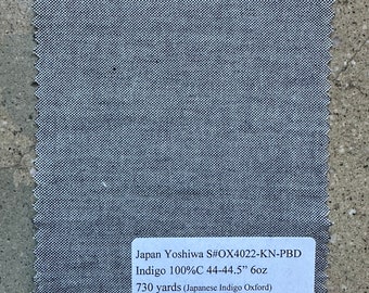 May include: A square swatch of indigo fabric with a textured weave and a jagged edge. The label reads "Japan Yoshiwa S#OX4022-KN-PBD Indigo 100%C 111.76-113.03cm 6oz 667.59m (Japanese Indigo Oxford)".