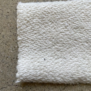 May include: Close-up of a white, textured fabric with a soft, fuzzy appearance. The fabric has a slightly uneven surface, creating a subtle pattern.