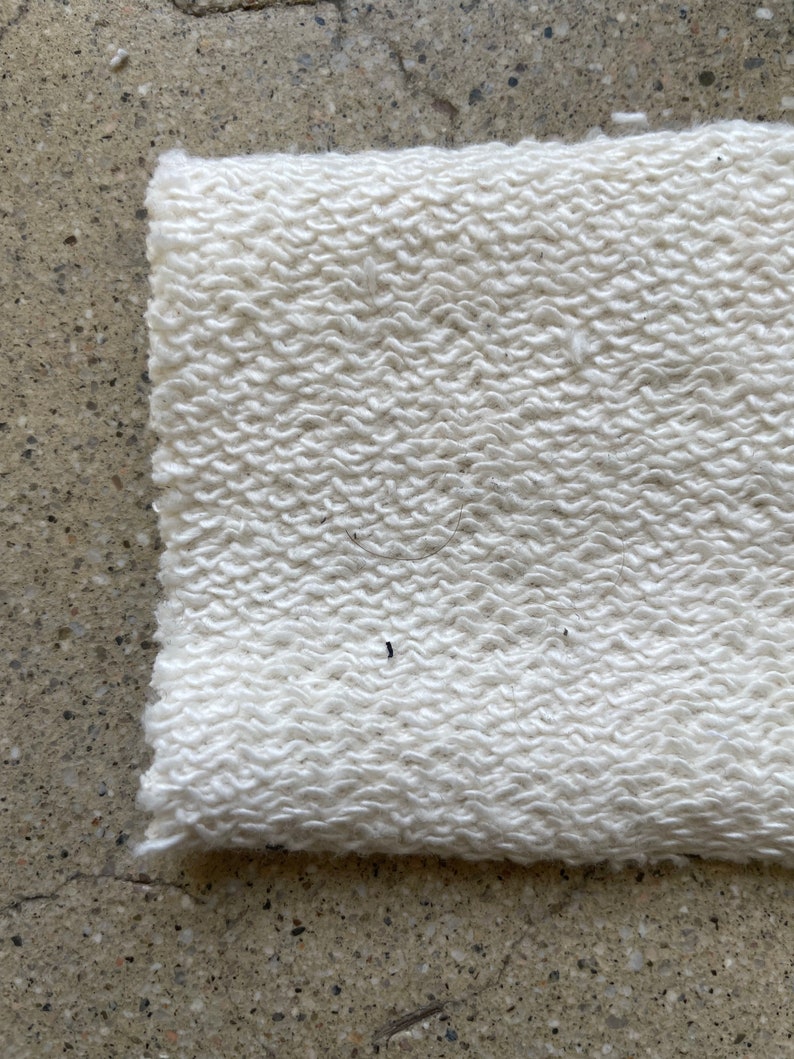 May include: Close-up of a white, textured fabric with a soft, fuzzy appearance. The fabric has a slightly uneven surface, creating a subtle pattern.