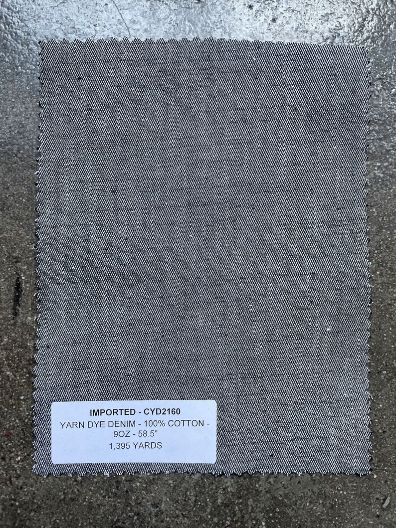 May include: A gray denim fabric swatch with a white label that reads "IMPORTED - CYD2160 YARN DYE DENIM - 100% COTTON - 9OZ - 58.5" 1,395 YARDS"