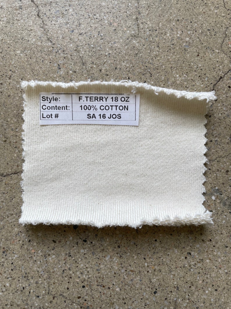 May include: A close-up of a white fabric swatch with a label that reads "Style: F.TERRY 18 OZ, Content: 100% COTTON, Lot #: SA 16 JOS".