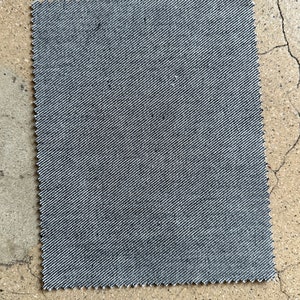 May include: A close-up of a gray denim fabric swatch. The fabric has a subtle diagonal weave pattern.
