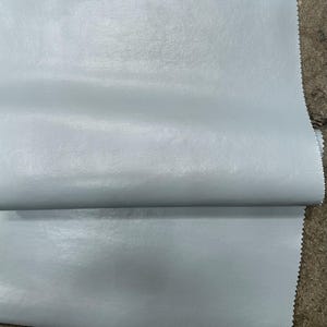 May include: A close-up of a light blue faux leather fabric. The fabric has a smooth, slightly textured surface.