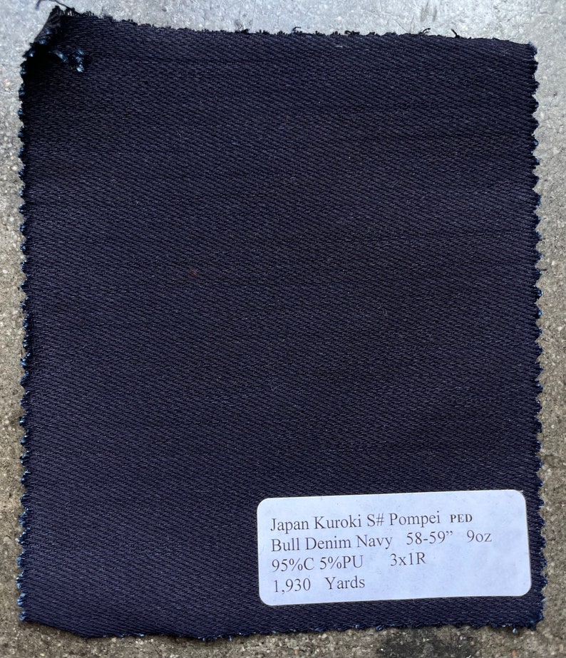 May include: A dark blue denim fabric swatch with a white label that reads "Japan Kuroki S# Pompei PED Bull Denim Navy 58-59" 9oz 95%C 5%PU 3x1R 1,930 Yards".