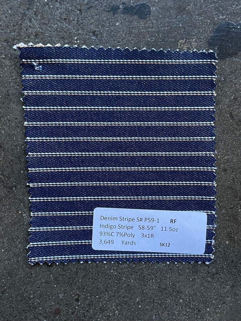 K&ouml;nnte beinhalten: Ein Muster aus Indigo-Streifen-Denimstoff mit wei&szlig;en Streifen. Der Stoff besteht aus 93 % Baumwolle und 7 % Polyester. Der Stoff ist 58-59 Zoll breit und wiegt 11,5 Unzen pro Yard. Der Stoff ist ein 3x1-Rechts-K&ouml;pergewebe. Es sind 3.649 Yards Stoff verf&uuml;gbar. Der Stoff ist mit dem Code P59-1 und dem Code SK12 gekennzeichnet.