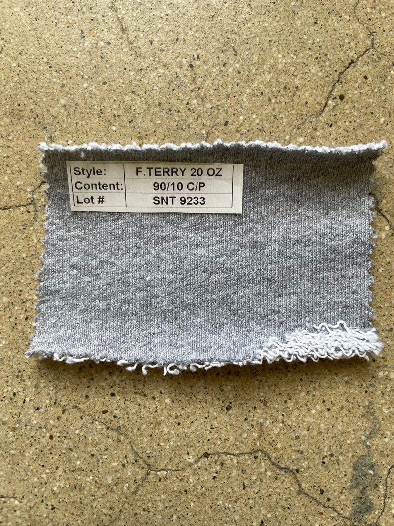 May include: A close-up of a gray fabric swatch with a white label that reads "Style: F.TERRY 20 OZ", "Content: 90/10 C/P", and "Lot #: SNT 9233".