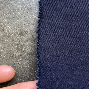 May include: Close-up of a dark blue fabric with a textured weave. The fabric has a raw edge.