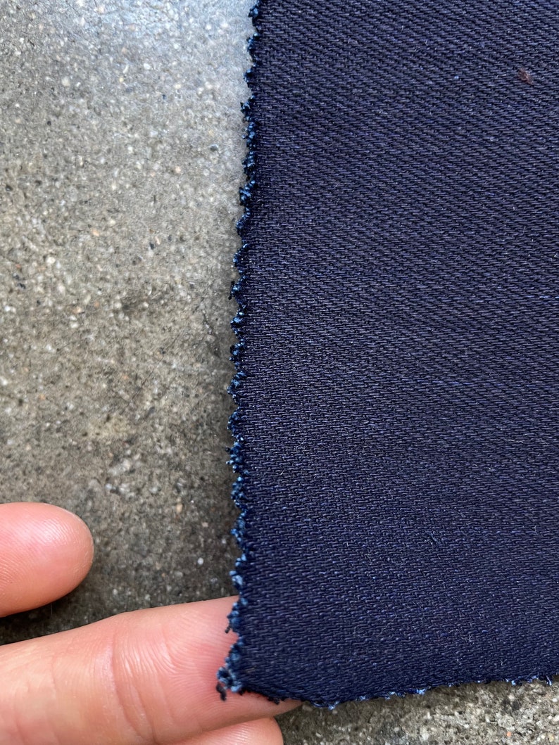 May include: Close-up of a dark blue fabric with a textured weave. The fabric has a raw edge.