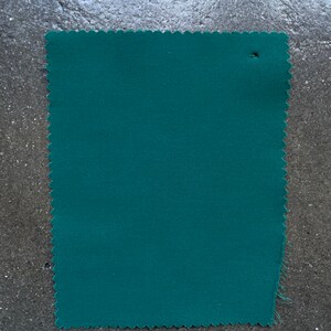 May include: A solid teal green fabric swatch with a slightly rough texture.