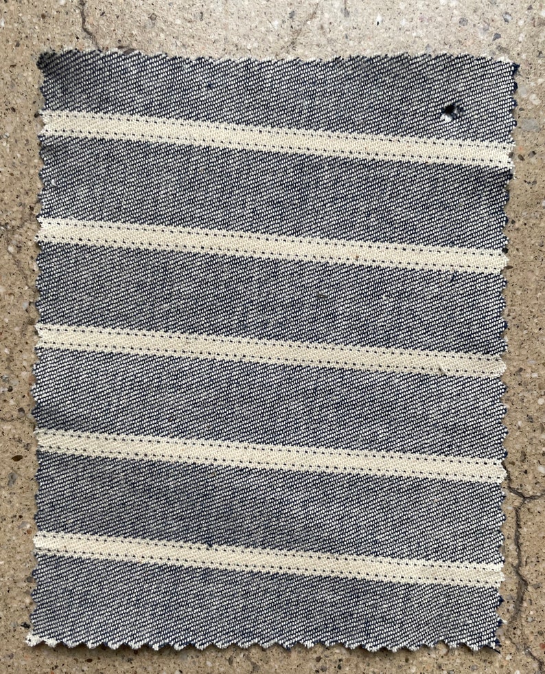 Puede incluir: Primer plano de una tela de rayas azules y blancas con un patr&oacute;n diagonal. La tela tiene un tejido texturizado y un borde ligeramente irregular.