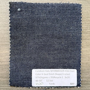 May include: A swatch of dark blue denim fabric with a textured surface. A white label provides details: Candiani Italy, Color K-Seal finish, 97% Organic, 48-50 inches, 12.5oz. The fabric is likely for apparel or home decor.