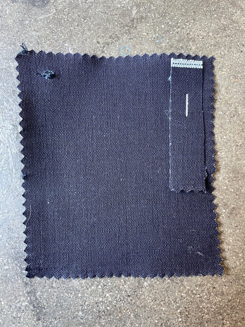 May include: A dark blue fabric swatch with a smaller swatch of the same fabric sewn to the right side. The fabric has a woven texture.