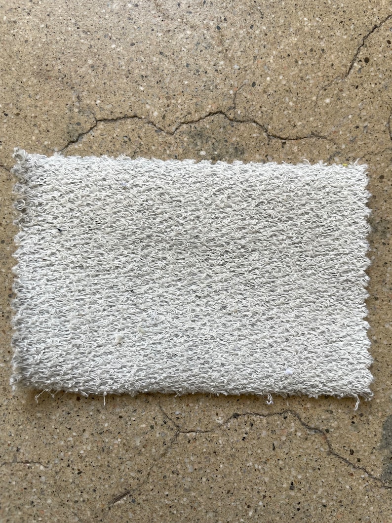 May include: A white, textured, rectangular fabric swatch. The fabric has a soft, fuzzy texture.